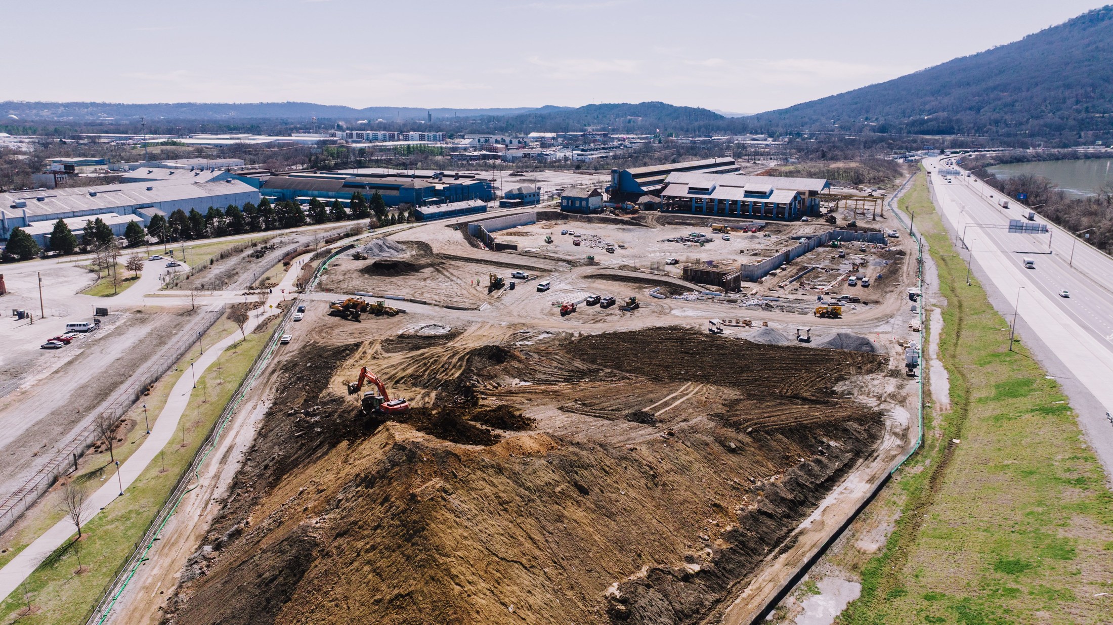 Aerial view of a construction site with earthmoving equipment, foundations, and surrounding buildings
